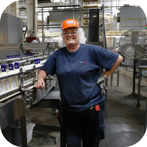A woman wearing a hairnet and hard hat standing in front of machinery in a factory.
