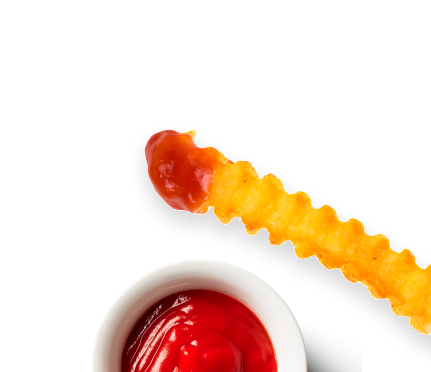 An image of a curly fry, dipped in tomato sauce, with a pot of tomato sauce below.