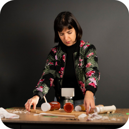A woman preparing food and bottles of sauce on a table in front of a camera and a set of lights.