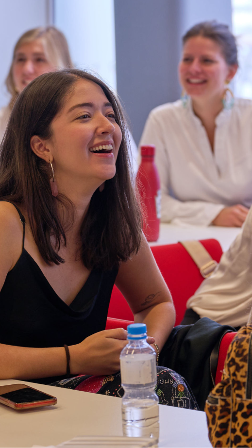 A woman, in a room full of people, seated at a table smiling