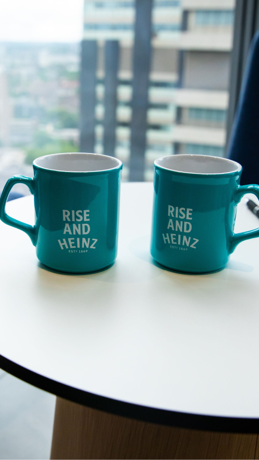 Two blue mugs on a table that read Rise and Heinz