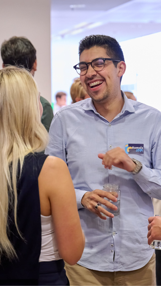 A man with glasses laughing in conversation with a colleague