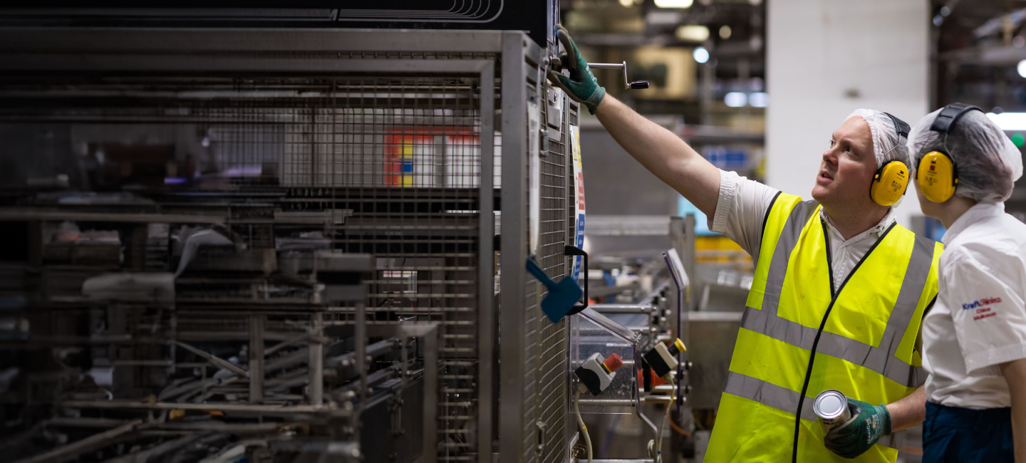Two men wearing ear defenders in a factory.