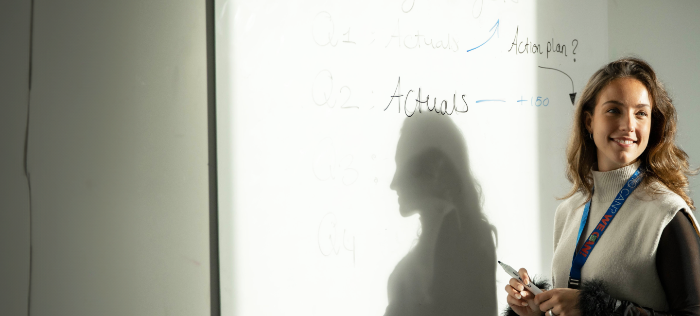 A woman is writing on a whiteboard and presenting.
